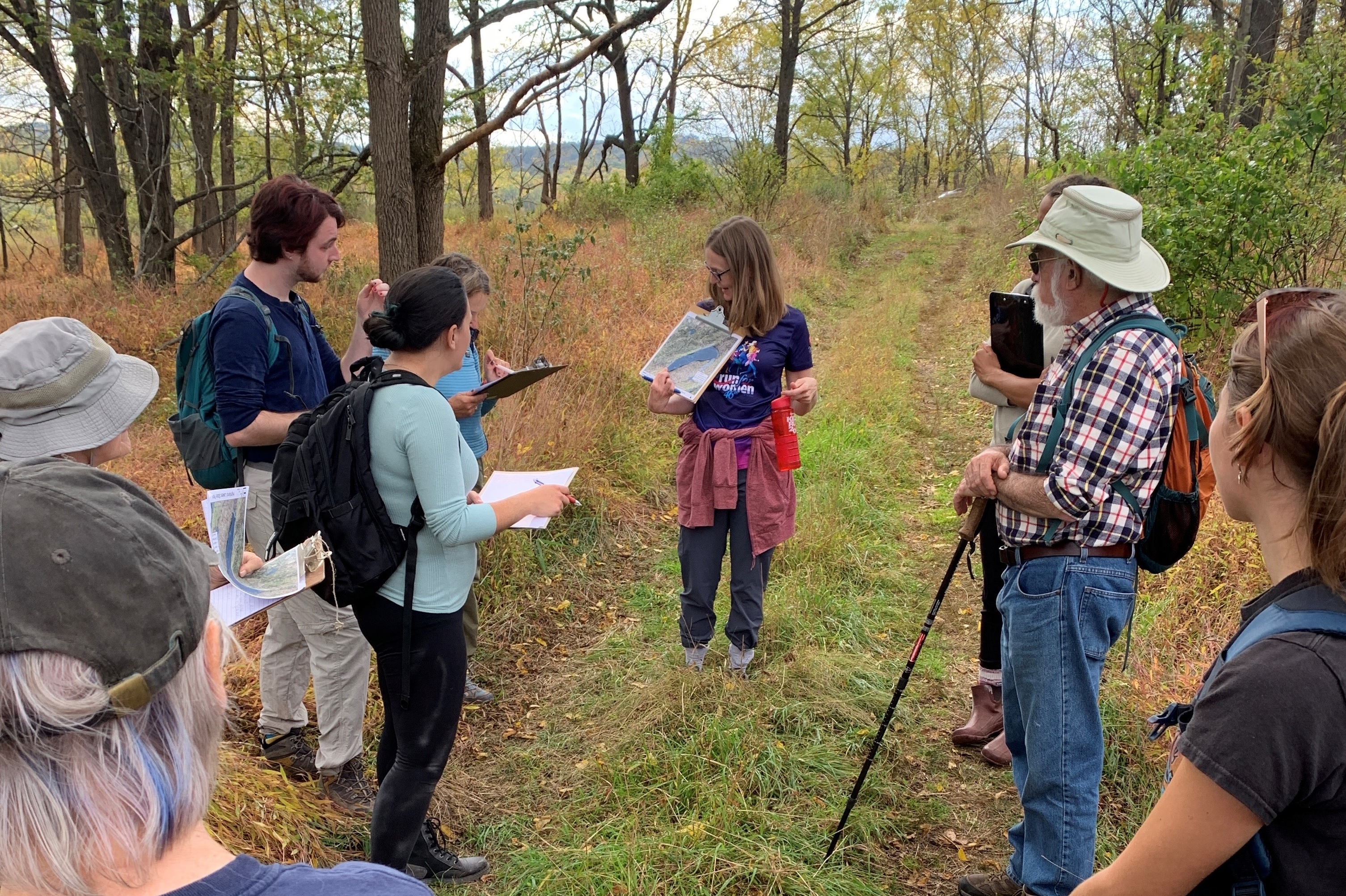 A group of people stand in a circle outdoors looking at maps.