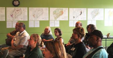 Residents sit and listen to a presentation with NRI maps hanging on the wall in the background