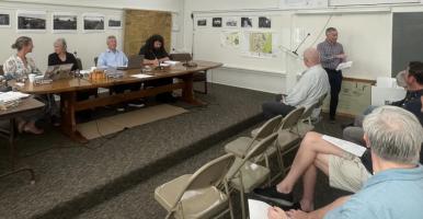 Town Hall meeting with board members and audience looking at man reading a resolution.