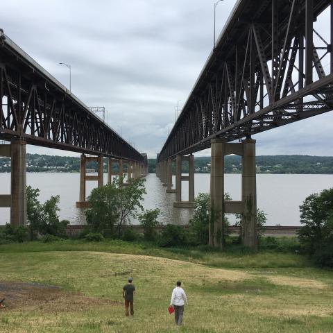 Two people walk toward the Hudson River in view of the Newburgh-Beacon bridge.