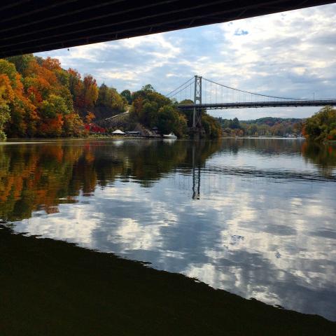 View of Rondout Creek, with clouds reflecting in water and views of Fall foliage and boats. By L Heady