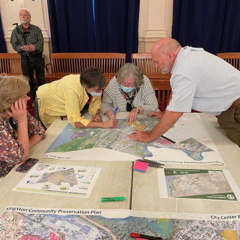 Individuals gather around a table looking at maps at the Kingston City Hall.
