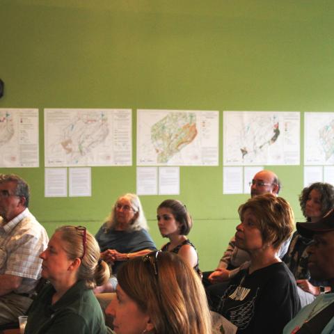 Residents sit and listen to a presentation with NRI maps hanging on the wall in the background