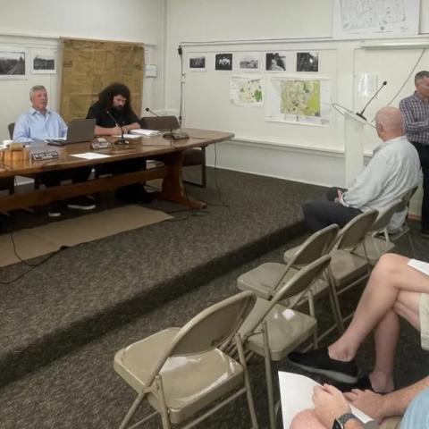 Town Hall meeting with board members and audience looking at man reading a resolution.